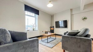 Een moderne woonkamer met een zithoek, een salontafel en een flatscreen televisie aan de muur.