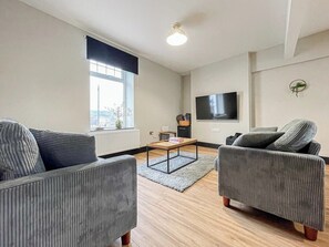 A modern living room with a sofa set, a coffee table, and a flat-screen TV mounted on the wall. - Chestnut House, modern base to explore and rest (Merthyr Tydfil County Borough)