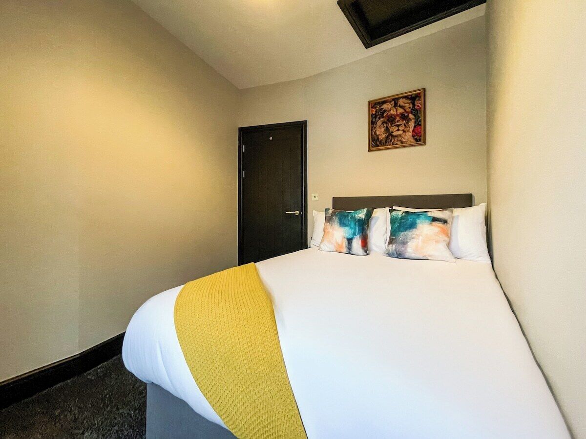 A hotel room with a bed, a door, and a painting on the wall.