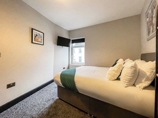 A bedroom with a bed, a window, a wall-mounted TV, and a framed picture.