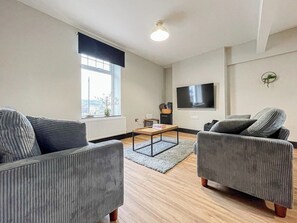Un salon moderne comprenant un canapé, un fauteuil, une table basse et un téléviseur à écran plat.