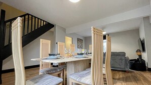 Een eetruimte met een tafel gedekt voor vier personen, omringd door stoelen met verticale latten. Een trap is op de achtergrond zichtbaar.