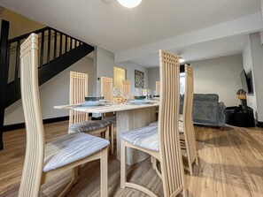 A dining area with a table set for four, surrounded by chairs with vertical slats. A staircase is visible in the background. - Chestnut House, modern base to explore and rest (Merthyr Tydfil County Borough)