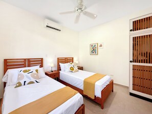 Ein Hotelzimmer mit zwei Betten, einem Deckenventilator, einer Klimaanlage und einer Tür mit Holzpaneelen.