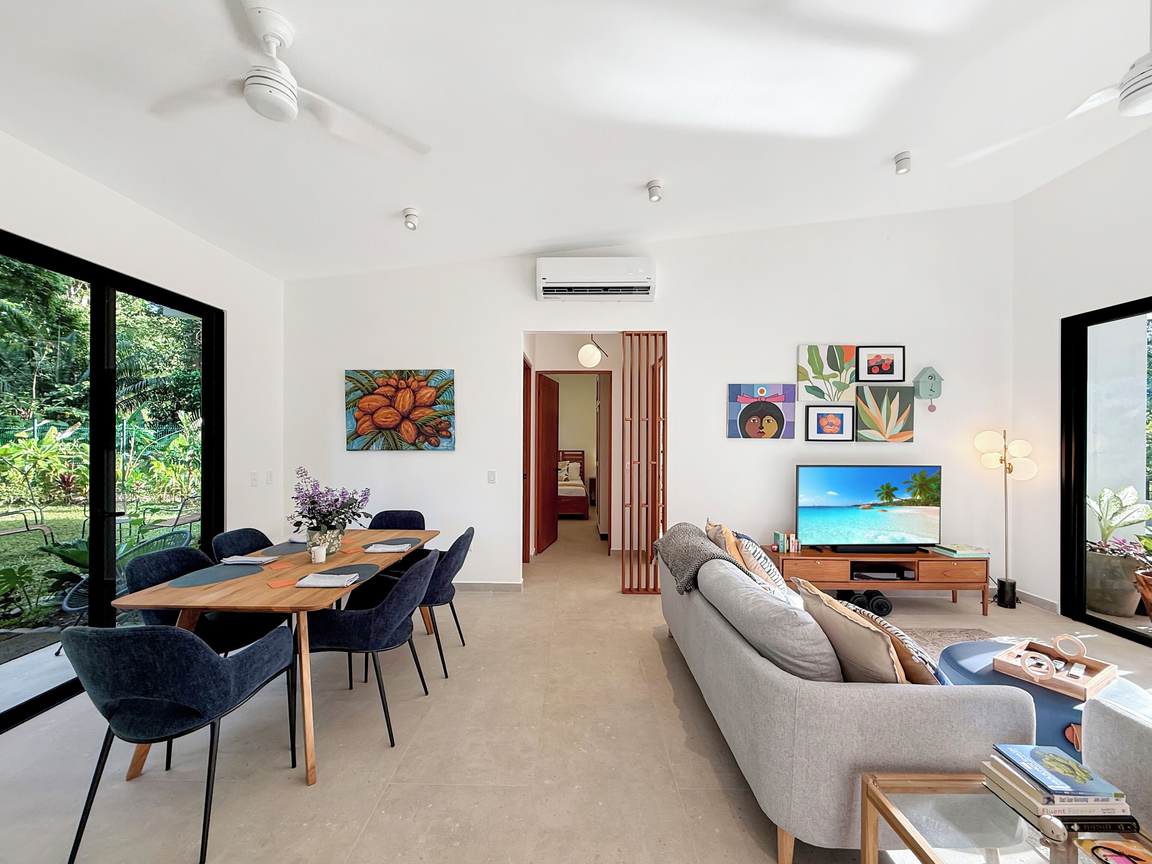 A modern living room with a dining area, a sofa, a TV, and artwork on the walls.