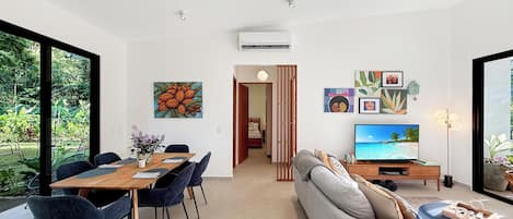 A modern living room with a dining area, a sofa, a TV, and artwork on the walls.