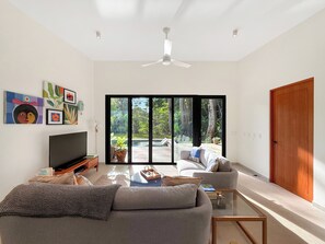 Ein modernes Wohnzimmer mit einer Couch, einem Couchtisch und einem Fernseher. Eine Glastür führt in einen Garten.
