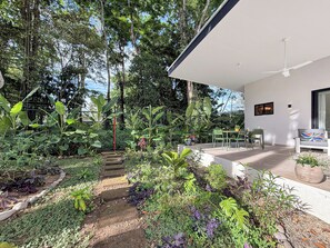 A modern outdoor patio with a dining area, surrounded by lush tropical plants and a staircase leading to a covered seating area. - Charming 3-bedroom house with AC in Playa Negra Playa Viejo (Playa Negra, Puerto Viejo de Talamanca)