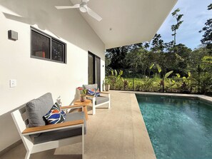 A poolside area with a white wall, a ceiling fan, and a view of a lush garden. - Charming 3-bedroom house with AC in Playa Negra Playa Viejo (Playa Negra, Puerto Viejo de Talamanca)