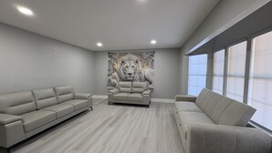 Un soggiorno moderno con un divano grigio, un murale decorativo raffigurante un leone e ampie finestre.