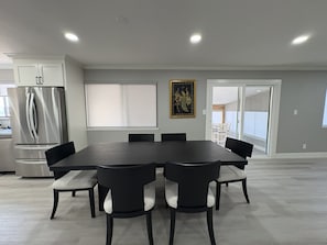Une cuisine moderne équipée d’un réfrigérateur en acier inoxydable, d’une table à manger avec six chaises et d’une grande fenêtre avec des stores.