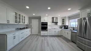 Una cucina moderna con mobili bianchi, elettrodomestici in acciaio inossidabile e una parete di fondo in marmo.