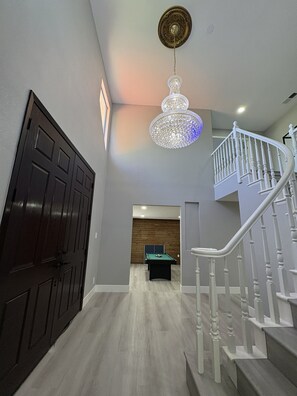 Un couloir avec une table de billard, une porte en bois et un escalier doté de rampes blanches.