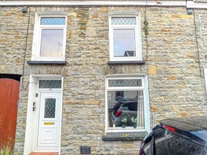 A stone building with three windows, a door, and a car parked in front.