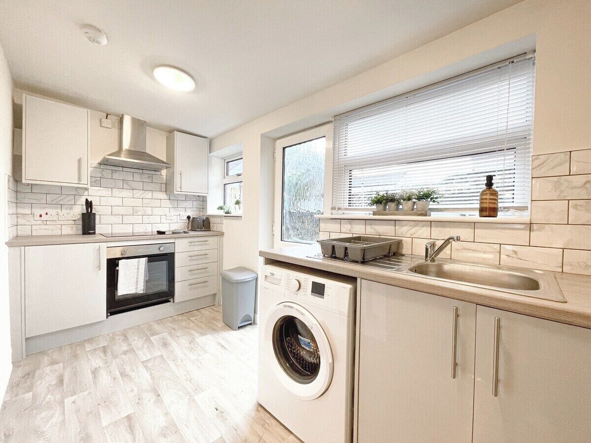 A compact kitchen with a built-in oven, washing machine, and a window with blinds.