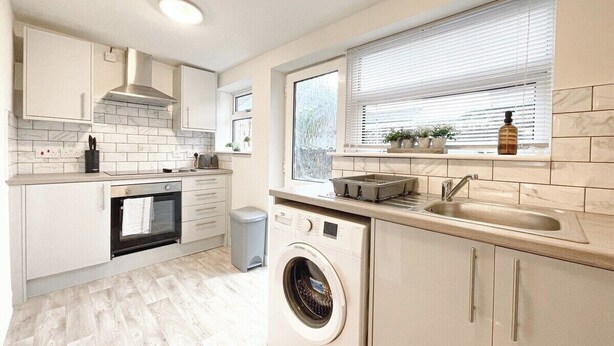 Eine kleine Küche mit Backofen, Waschmaschine und einem Fenster mit Jalousien.
