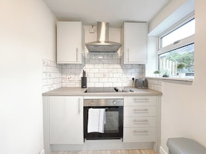 Cocina compacta con armarios blancos, extractor de acero inoxidable, horno empotrado y ventana con vista a follaje.