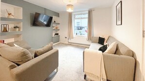 Ein Wohnzimmer mit Sofa, Fernseher und einem fensterbelaubten Fenster.