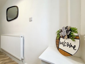 A hallway with a white radiator, a wall-mounted mirror, and a welcome sign with a bow and greenery.