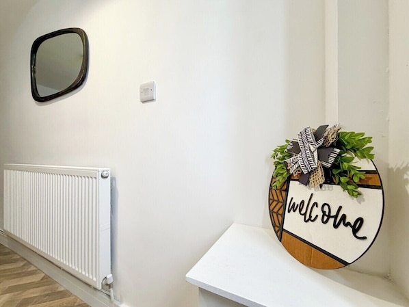A hallway with a white radiator, a wall-mounted mirror, and a welcome sign with a bow and greenery.