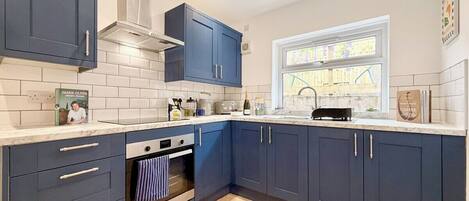 A modern kitchen with dark blue cabinets, a white countertop, and a herringbone-patterned floor.