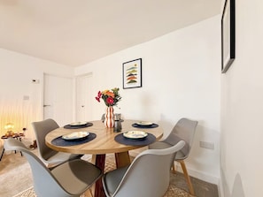 A dining area with a round table, six chairs, a vase with flowers, and a framed picture on the wall.