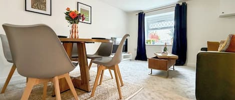 A modern living room with a dining area, featuring a sofa, chairs, a coffee table, and a view of the outdoors.