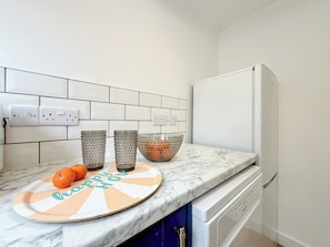 A kitchen with white tiled backsplash, a marble countertop, a white refrigerator, and a dish rack.
