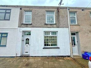 A two-story residential building with a white facade, a front door with a glass panel, and a small porch area. - Rowan | Stylish 3-Bed Home, Merthyr Tydfil (Merthyr Tydfil County Borough)