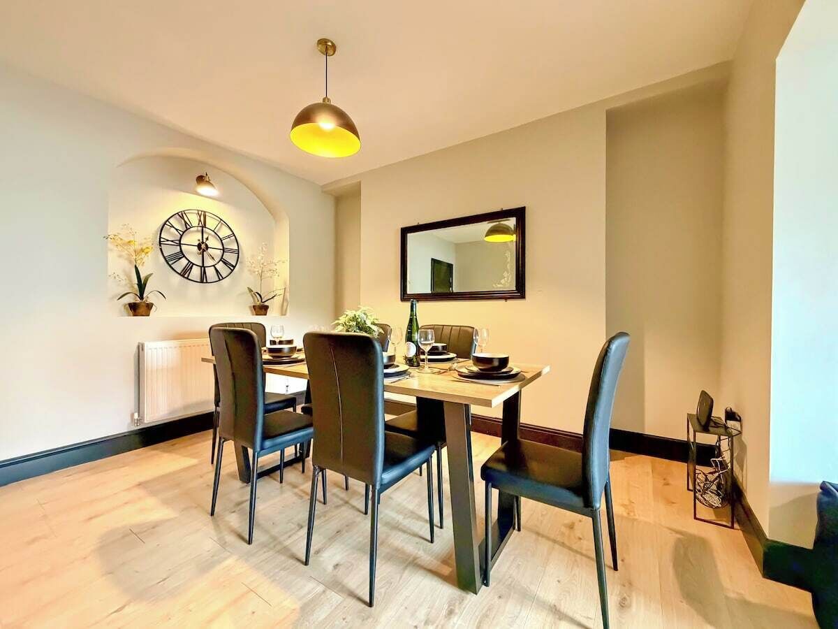 A dining area with a round table, four chairs, a wall clock, and a mirror.
