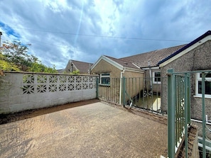 A residential property with a gravel driveway, a white decorative fence, and a green metal gate.