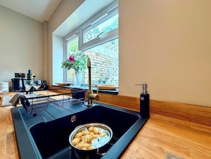 A kitchen with a black sink, a bowl of potatoes, a wine bottle, and a vase with flowers.