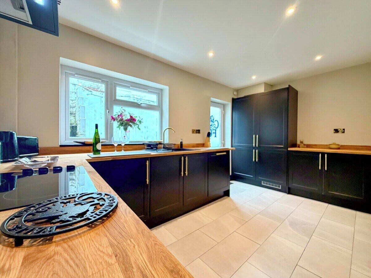 A modern kitchen with dark cabinetry, a wooden countertop, and a window providing natural light.