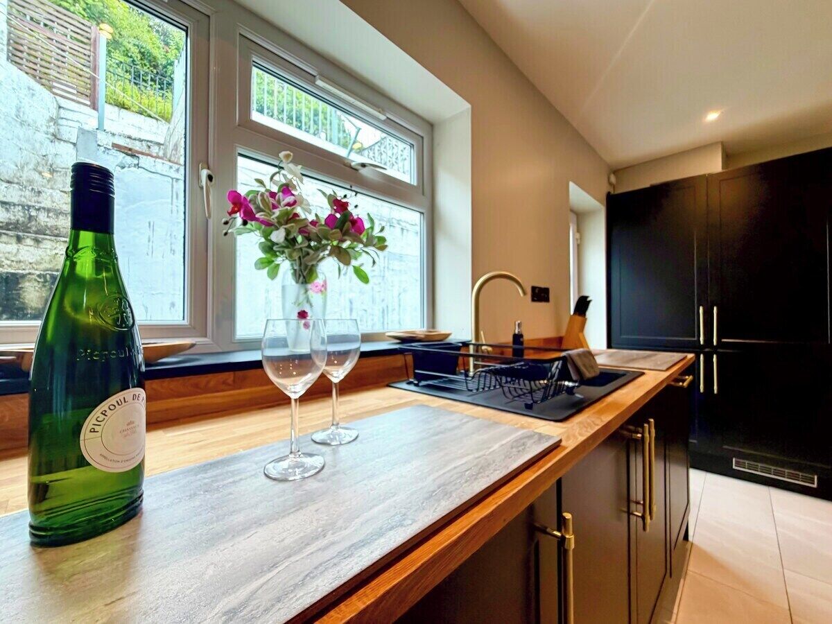 A modern kitchen with a wooden countertop, a wine bottle, two wine glasses, and a vase with flowers.