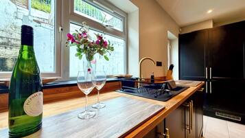 A modern kitchen with a wooden countertop, a wine bottle, two wine glasses, and a vase with flowers.