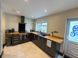 A modern kitchen with dark cabinetry, a wooden countertop, a built-in oven, and a window providing natural light.