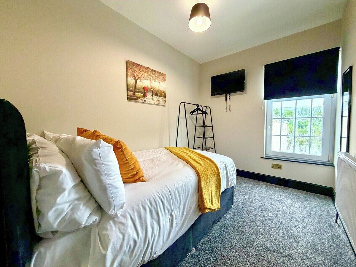 A bedroom with a bed, a window, a painting, and a TV.