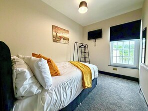 Un dormitorio con cama, ventana, un cuadro y televisor.