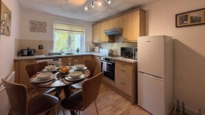 A modern kitchen with wooden cabinets, a white refrigerator, and a dining area with a table set for four.