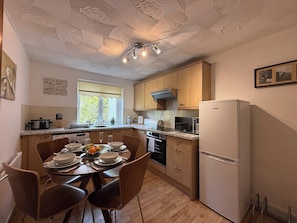 Una cocina moderna con armarios de madera, un refrigerador blanco y un comedor con una mesa dispuesta para cuatro.