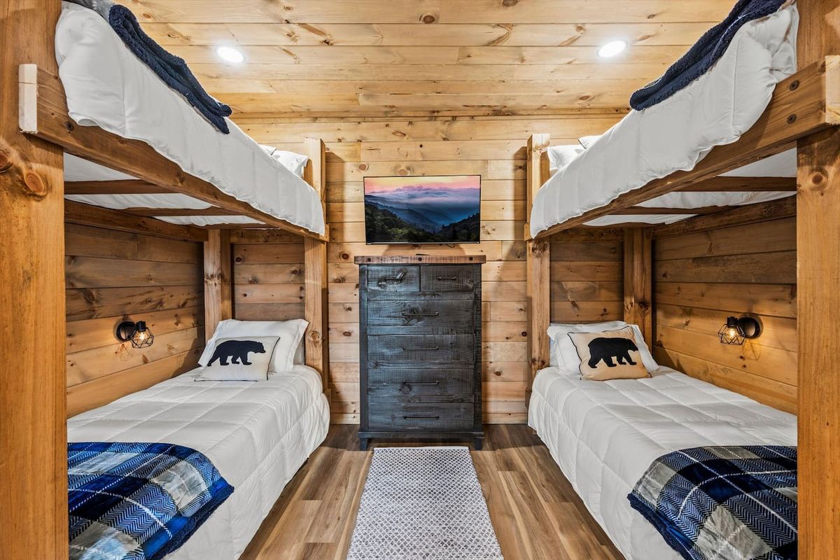 A cabin with two bunk beds, a central wooden door, and a wall-mounted picture.