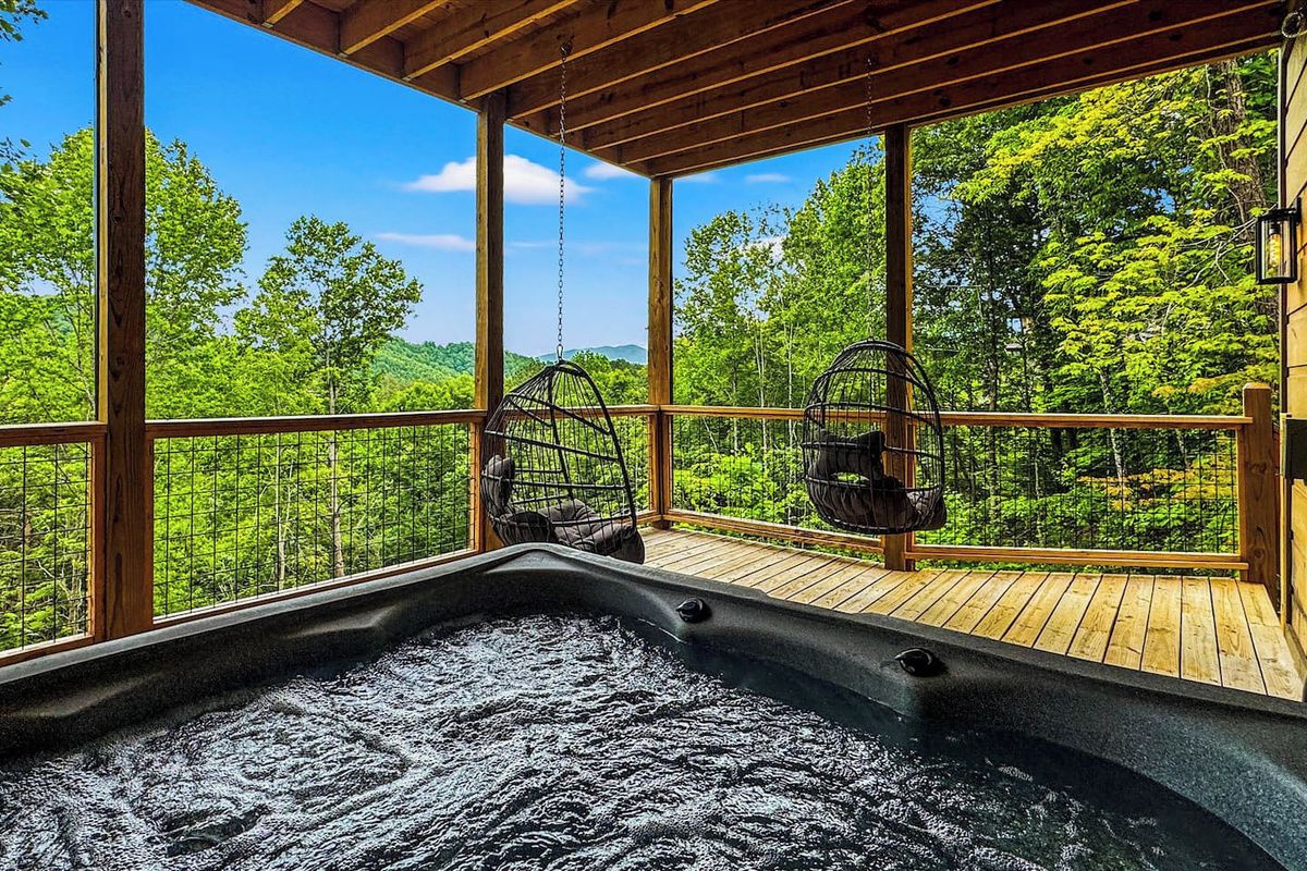 A hot tub with a wooden deck and large windows overlooking a forest.