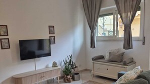 Een moderne woonkamer met een flatscreen-televisie, een bank, een lange bank en een raam met gordijnen.
