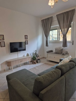 Ein modernes Wohnzimmer mit Fernseher, einer Couch, einer Bank und einem Fenster mit Vorhängen.