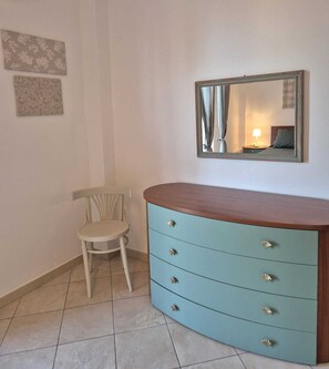 Ein Zimmer mit einem hellblauen Schminktisch, einem Sessel, einem wandmontierten Spiegel und zwei gerahmten Bildern.