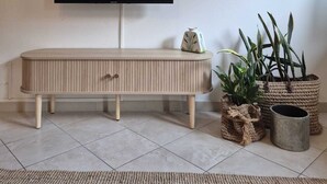 Een woonkamer met een flatscreen televisie aan de muur, een houten console en verschillende potplanten.