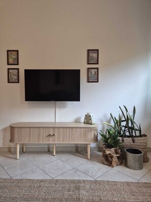 A living room with a flat-screen TV mounted on the wall, a wooden console table, and several potted plants. - Ella Home: Spacious Apartment with Terrace - Downtown Taormina (Taormina)