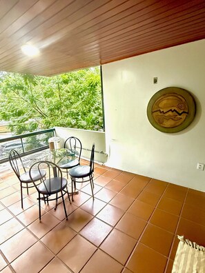 A balcony with a table and chairs, a view of greenery, and a decorative plate on the wall. - Raridade Ape 4 Quartosmeirelesbeira Mar180m2 (Fortaleza)