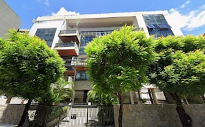 A multi-story building with balconies, a stone wall, and trees in front. - Raridade Ape 4 Quartosmeirelesbeira Mar180m2 (Fortaleza)