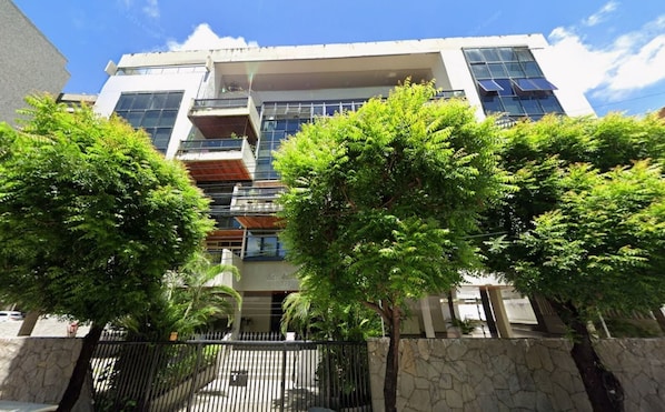A multi-story building with balconies, a stone wall, and trees in front. - Raridade Ape 4 Quartosmeirelesbeira Mar180m2 (Fortaleza)